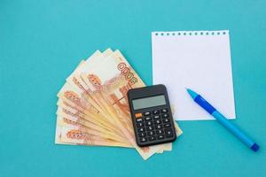 concepto de negocio. bloc de notas, dinero y calculadora en mesa azul foto