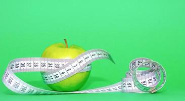 manzana verde con cinta métrica gris sobre fondo verde en el concepto de alimentación y dieta saludable foto