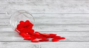 crystal wine glass filled with silk hearts on a light, wooden background. Valentine's Day holiday concept. photo