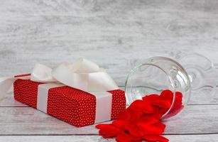 caja de regalo roja con patrón de guisantes, cinta blanca y corazón sobre fondo de madera. concepto de vacaciones, día de san valentín. foto