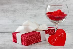 vidrio con corazones y una caja de regalo roja con un lazo blanco sobre un fondo de madera. concepto de vacaciones foto
