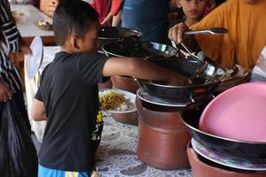 a child is waiting in line for food in front of which there is a large container to put vegetables made of clay.18 03 2022. photo