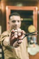 Young barber holding scissors in foreground. Vintage barber shop. photo