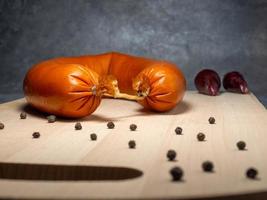 The sausage lies on a kitchen board with pepper photo