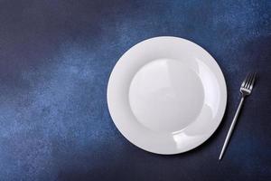 Empty white plate on blue background table. Flat lay photo