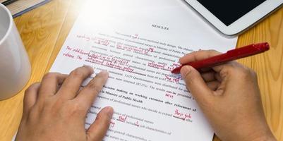 hand holding red pen over proofreading text photo