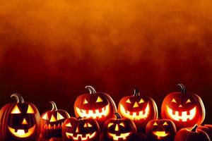 una fila de calabazas de halloween jack olantern talladas a lo largo de la parte inferior de la imagen contra un fondo grunge naranja oscuro foto