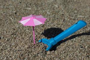 Toy pink umbrella and blue spade on the beach. Travel and holidays with children.
