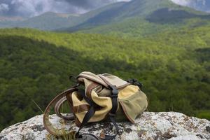una mochila marrón-verde se encuentra sobre una gran piedra gris sobre una roca con el telón de fondo de montañas verdes. foto