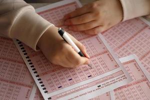 llenando un boleto de lotería. una joven juega a la lotería y sueña con ganar el premio mayor. mano femenina marcando el número en el billete de lotería rojo foto