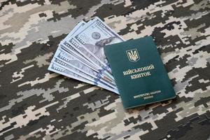 Ukrainian military ID and US dollar bills on fabric with texture of pixeled camouflage. Cloth with camo pattern in grey, brown and green pixel shapes with Ukrainian army personal token. photo