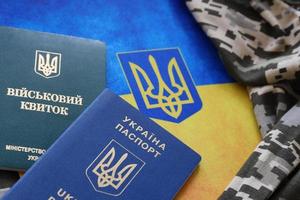 Ukrainian military ID and foreign passport on fabric with texture of pixeled camouflage. Cloth with camo pattern in grey, brown and green shapes with Ukrainian army personal token and passport. photo