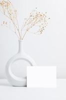 vista frontal de la tarjeta de felicitación y flor seca en jarrón de cerámica sobre la mesa