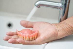 anciana asiática o anciana paciente sosteniendo y lavando dentadura postiza en la sala del hospital de enfermería foto