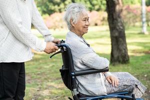 Caregiver help and care Asian senior or elderly old lady woman patient sitting and happy on wheelchair in park, healthy strong medical concept. photo