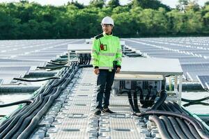 electricista masculino con casco de seguridad blanco parado en una escalera y montando un panel solar fotovoltaico bajo un hermoso cielo azul. concepto de fuentes alternativas de energía. foto