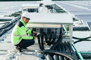 Closed-up of Male electrician in white safety helmet standing on ladder and mounting photovoltaic solar panel under beautiful blue sky. photo