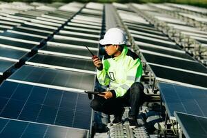 Plano medio de ingenieros sentados en el techo inspeccionando y revisando el panel de celdas solares sujetando la caja del equipo y la comunicación por radio foto