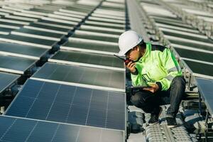 Medium shot of Engineers sitting on roof inspect and check solar cell panel ecology energy sunlight alternative power factory concept. by hold equipment box and radio communication photo