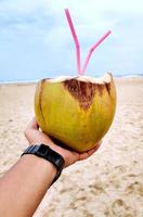 mano masculina con un coco en la playa foto