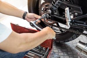 Mechanic using a wrench and socket to Remove and Replace Rear Motorcycle Wheel, working in garage maintenance, repair motorcycle concept  .selective focus photo