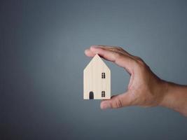 concepto de vender una casa. una mano sostiene una casa modelo sobre un fondo gris. agente de bienes raíces ofrece casa, seguro de propiedad y seguridad, conceptos de vivienda asequible, vendedor. foto