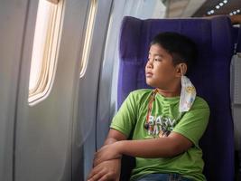 An Asian boy sits and smiles and looks out the window of an airplane. photo