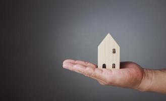 Concept of selling a house. A hand is holding a model house on a gray background. Real estate agent offer house, property insurance and security, affordable housing concepts. photo