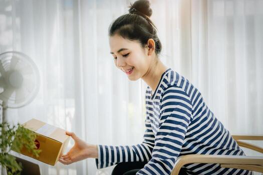 Online merchandising business idea, beautiful girl holding a parcel delivery box and using a computer to input Track And Trace parcel numbers to customers. photo