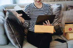 Online merchandising business idea, beautiful girl using tablet computer to check orders to deliver parcels to customers according to orders received from customers. photo