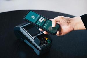 concepto de tecnología de pago seguro y cargo por servicio, los clientes están usando su teléfono para pagar usando tecnología paywave tocando cerca de la terminal de tarjeta electrónica. foto