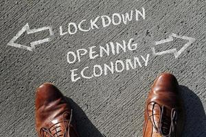 Two leather shoes in front of the words Lockdown and Opening Economy and arrows pointing into opposite directions photo