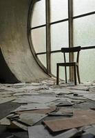 Chair in front of a round window in an abandoned church with papers and book pages lying on the ground photo