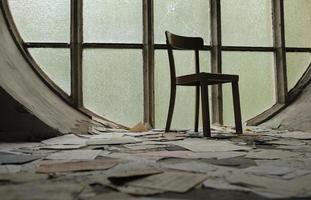 silla frente a una ventana redonda en una iglesia abandonada con papeles y páginas de libros en el suelo foto