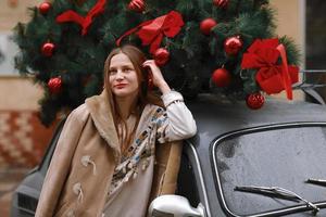 chica en un paseo de invierno en la ciudad, nieve, afuera. calle de invierno en la ciudad. niña feliz camina por la ciudad el día de navidad. coche de navidad con un regalo. feliz Año Nuevo y feliz Navidad. foto