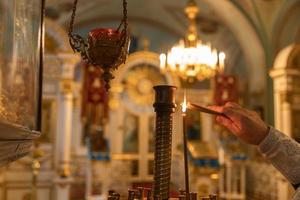Iglesia Ortodoxa. cristiandad. mano del sacerdote encendiendo velas encendidas en la iglesia ortodoxa tradicional en la víspera de pascua o navidad. religión fe orar símbolo. foto