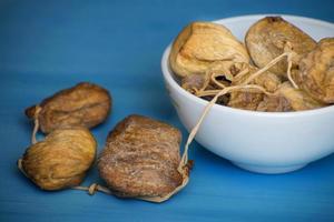 Dried figs in a white bowl on a blue table. Dried fruit. photo