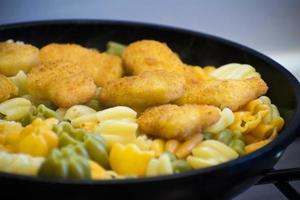 pasta con nuggets de pollo en una sartén. nuggets de pollo frito. sabrosos y crujientes nuggets de pollo. Menu de niños. foto