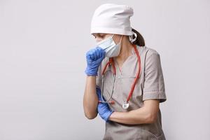 enfermera con ropa de trabajo protectora, máscara médica, estetoscopio y tos durante la epidemia de coronavirus sobre fondo blanco foto