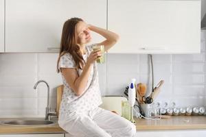 Beautiful girl drinks freshly prepared smoothie in kitchen. smoothies freshly made from assorted vegetable ingredients on kitchen counter. Healthy Eating. selective focus photo