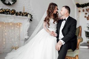 Young couple in love bride and groom posing in studio on background decorated with Christmas tree in their wedding day at Christmas. Enjoy a moment of happiness and love. photo