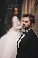 Wedding couple near the vintage green door. Stone walls in ancient town background. bride with long hair in lace dress and groom in suit and bow tie. Tender embrace. Romantic love photo