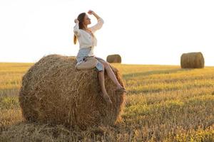 Portrait of beautiful girl on haystack roll on harvested wheat field in the summer. Selective focus. photo