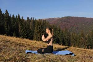 niña haciendo ejercicio de fitness de yoga al aire libre en el hermoso paisaje de las montañas. amanecer de la mañana, pose de loto namaste. meditacion y relajacion foto