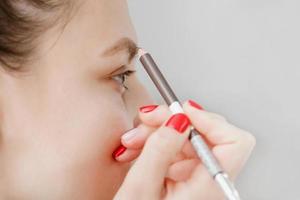 woman paints eyebrows in front of mirror. Beautiful girl paint eyebrows brown. Girl doing makeup in front of a mirror. The girl was caring for her face. photo