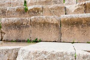 números griegos antiguos en asientos de piedra en el antiguo gran teatro del sur, jerash foto