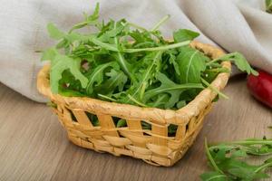 ruccola en una cesta sobre fondo de madera foto