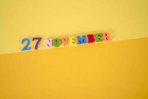 November 27 on a yellow and paper background with wooden and multicolored letters with space for text. photo