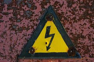 Old, rusty warning about danger and high voltage in form lightning yellow background. photo