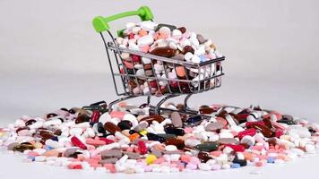 Metal decorative small shopping cart with green handles rotates on a white background. Being filled with tablets. Lots of pills in the cart and nearby. video